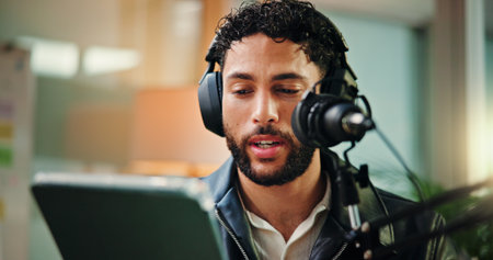 Talking, influencer and man with mic, tablet or reading script for episode, content creation or app. Live streaming, podcaster and person with tech for entertainment, online and host with headphonesの写真素材