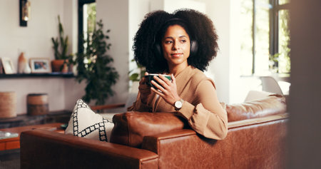 Home, thinking and woman with coffee, headphones and relax with break, audio and live streaming. Apartment, headset and person on couch, radio and listening to music, daydreaming and sound with teaの写真素材