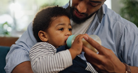 Home, father and baby with bottle, feeding and bonding together with nap time, wellness and care. Toddler, parent and dad with infant, child development and health with nutrition, growth and loveの写真素材