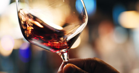 Hand, person and swirl red wine in glass for taste testing, quality control and sensory ritual. Customer, inspection and alcohol for aroma, balance flavour and evaluation process and event with bokehの写真素材