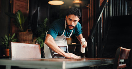 Cleaning, spray bottle and wipe with man in coffee shop for disinfection, hospitality or hygiene. Bacteria, dirt and table with waiter in cafe or restaurant for maintenance of small business startupの写真素材