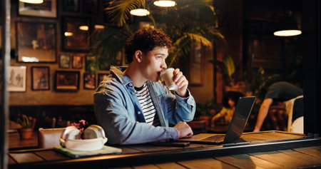 Drinking, coffee and man with laptop, cafe and remote work at night, copywriter and research on web. Working late, freelancer and person with tea in shop, thinking and tech for article or projectの写真素材