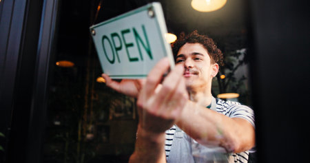 Open sign, small business and window with waiter in coffee shop for hospitality, retail or service. Entrance, happy and opening with man in cafe or restaurant for startup announcement or signageの写真素材