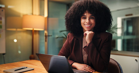 Laptop, night and portrait with woman accountant in office for finance, investment or report deadline. Business, computer and financial review with smile of happy African employee at workplace deskの写真素材