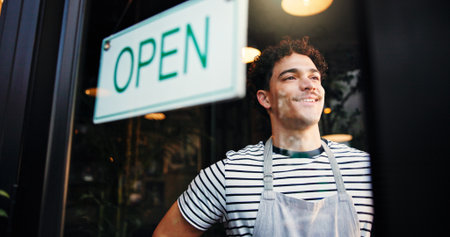 Open sign, small business and window with man in coffee shop for hospitality, retail or service. Entrance, opening and smile of waiter in cafe or restaurant for startup announcement or signageの写真素材