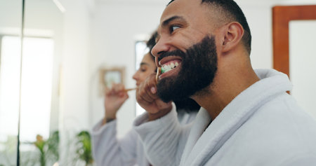 Man, brushing teeth or mirror in bathroom for dental hygiene, wellness or morning in home. Male person, oral care or reflection with toothbrush for routine, cleaning mouth or gum health in houseの写真素材