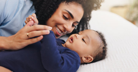 Mother, happy and playing with baby on bed for bonding together, motherhood or connection. Security, family and woman relax with infant in home for protection, morning routine and child developmentの写真素材