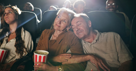 Senior couple, popcorn and sleep at movie theater with smile in crowd, bonding and show on date. Elderly people, relax together and love with fast food, snack and care with film screening at cinemaの写真素材