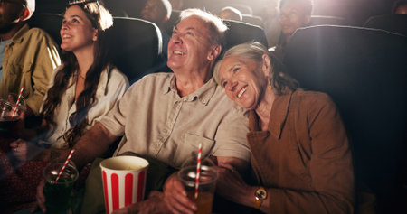 Senior couple, laugh and happy at cinema for movie in crowd, bonding and date with comedy show. Elderly people, smile and excited with fast food, popcorn and watch comic film with love at theaterの写真素材