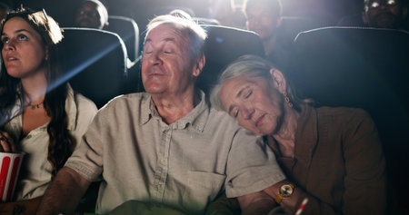 Senior couple, date and sleep at movie theater in crowd, bonding or tired with rest at show in. Exhausted elderly people, relax together and love with fatigue, embrace and film screening at cinemaの写真素材
