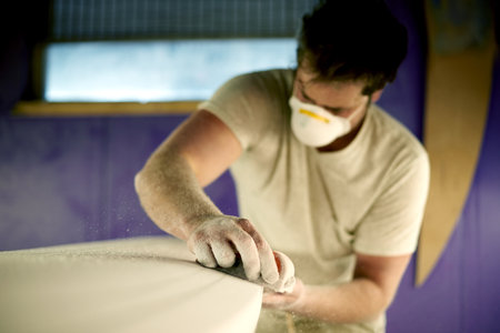 Hands, sanding and surfboard with man in workshop for fixing, maintenance or repair. Design, production and sandpaper with person in small business or surf shop studio for manufacturing processの写真素材