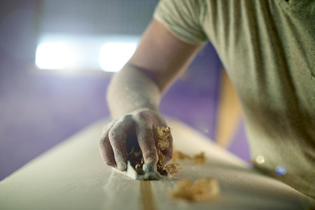 Manufacturing, hand and person with planer on surfboard for production process, polish and creative craftsmanship. Surfer, blank and tools for shape, design and shaving wood surface in workshopの写真素材