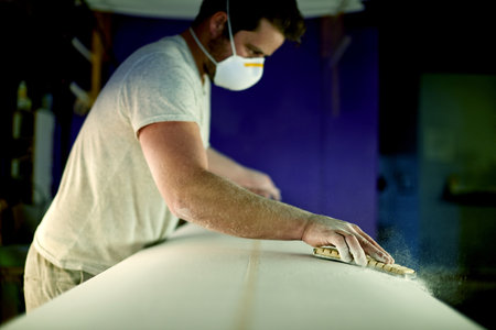 Sanding, mask or man with woodwork project for manufacturing furniture or surfing equipment. Workshop, small business or creative worker in labor production process to building surfboard in warehouseの写真素材