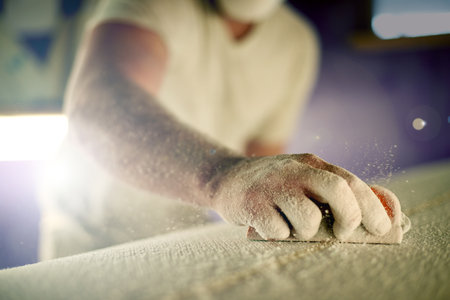 Manufacturing, hand and sanding surfboard in workshop for production process, design and creative craftsmanship. Surf, worker and man with tools for shape, polish and grinding foam with dust closeupの写真素材