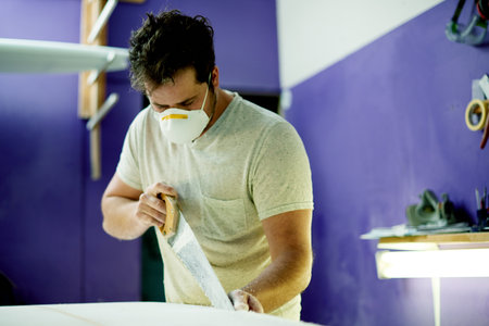 Man, saw and craftsman with foam, surfboard and PPE for skills, talent or hobby safety. Creative person, artist or entrepreneur with workshop for design manufacturing or custom work for artisan craftの写真素材