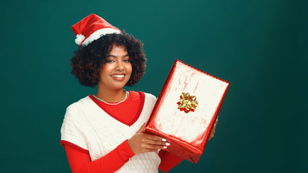 Christmas hat, portrait and black woman with gift in studio for tradition, festive or celebration. Happy, holiday and African female person with present box for xmas event by green background.の写真素材