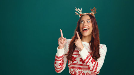 Christmas, excited woman and pointing up to space in studio for advertising, marketing or mockup. Laugh, offer or person with show promo, xmas discount or festive sale on holiday on green backgroundの写真素材