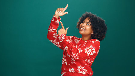 Christmas, pointing and smile with woman in studio for holiday season, celebration and promotion. Festive deals, xmas event and announcement with person on green background space for mockup and offerの写真素材