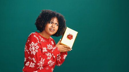 Curious, gift box and black woman in studio for christmas tradition, festive or surprise secret santa. Giveaway, mockup space and African person with xmas present for holiday by green background.の写真素材