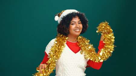 Woman, Christmas tinsel and portrait in studio, happy and Santa hat with decoration on background. Girl, smile and festive celebration with xmas cap, mock up space and holiday season in Costa Ricaの写真素材