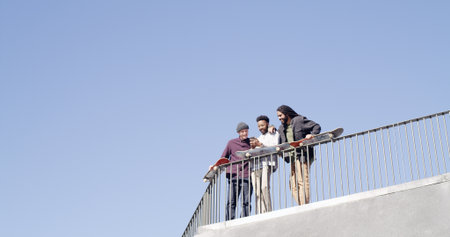 Below, friends and together with skateboard, phone and bonding on blue sky space. Conversation, people and gen z skater group with tech, smile and social media for fitness hobby and break for sportの写真素材
