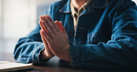 Faith, hands and prayer journal with person at desk in home for belief, confession or religion. Notebook, praying and study with spiritual man learning about God or Jesus in living room of apartmentの写真素材
