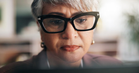 Glasses, reading and business woman on computer for insurance policy, report or research. Tech, office and serious face of mature accountant with email for claims update, risk management or proposalの写真素材