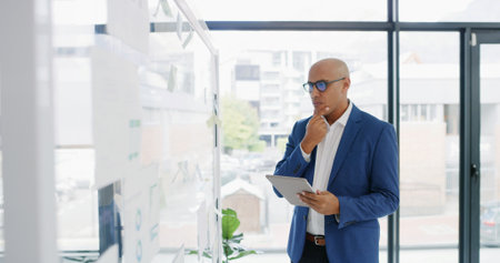 Businessman, tablet and thinking for finance, glass wall or brainstorming in office for strategy. Planning, employee and technology with sticky note, research or schedule tasks for investment projectの写真素材