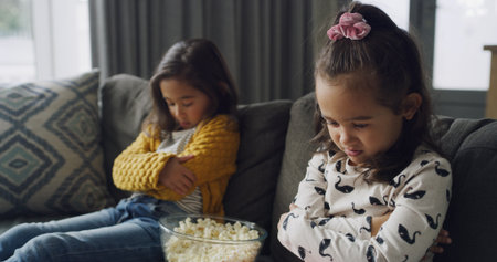Sad girl, siblings or conflict with popcorn on sofa for fight, argument or disagreement in home. Child, kids or upset sisters with attitude or behaviour for difference or living room dispute in houseの写真素材