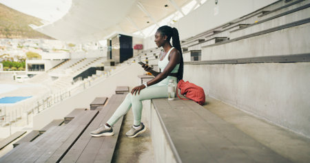 Athlete, black woman and relax with phone at stadium for social media, fitness app and event agenda. Female person, rest and mobile for texting, sports progress results and information for tournamentの写真素材