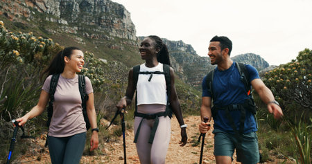 Friends, hiking and laughing in nature for travel, walking and group talking on vacation. Man, women and outdoor with trekking pole for adventure, funny joke and explore mountain path on journeyの写真素材