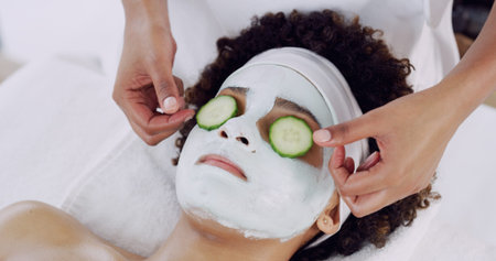 Woman, mask and cucumber at spa with hands, relax or skin treatment with care at lodge. Girl, rest...