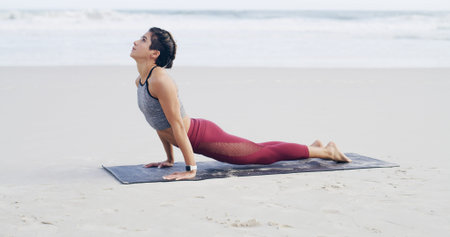 Beach, stretching and woman on mat, yoga or flexibility for muscle strength, awareness and wellness. Outdoor, upward facing dog and person with routine for fitness, space and balance in nature or seaの写真素材