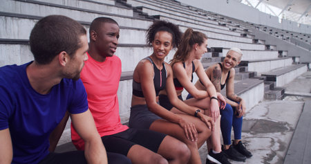 Conversation, fitness and rest with friends on stadium bleachers for bonding or sports training. Break, exercise and recovery with group of athlete people speaking in venue for workout discussionの写真素材