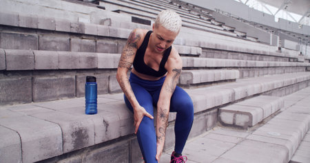 Rest, runner and woman with injury in stadium for workout, exercise and muscle fatigue for running. Fitness, sports track and person massage legs for accident, strain and pain for training outdoorの写真素材