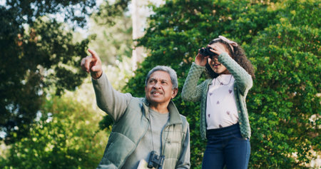 Grandfather, child and binocular in park for travel, sightseeing and pointing with view for bonding. Man, girl and explore for adventure, bird watching or fun together in nature with family in Mexicoの写真素材