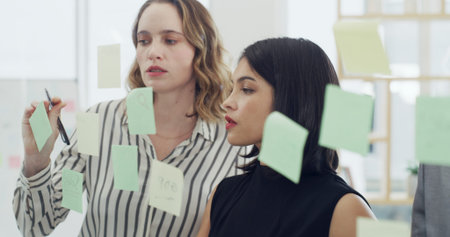 Sticky notes, discussion and business people in office for planning with creative project together. Meeting, research and team of editors with glass wall for brainstorming for publishing in workplaceの写真素材