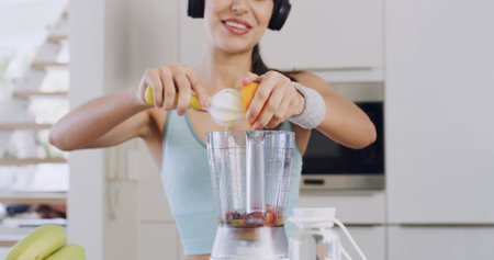 Headphones, smoothie and hands of a woman for healthy diet, nutrition and fruit in kitchen. Orange juice, blender and female person with vegan ingredients for drink, shake or streaming music in homeの写真素材