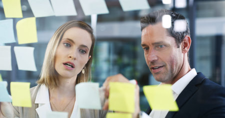 People, writing and sticky notes on glass in office for planning, schedule and financial ideas....