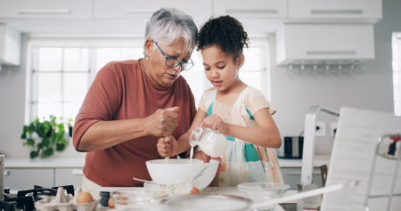 Baking, bowl and grandma with child in kitchen for learning, teaching and helping for cookies. Family, home and grandmother with girl with milk, ingredients and bonding for dessert, cake and pastryの写真素材