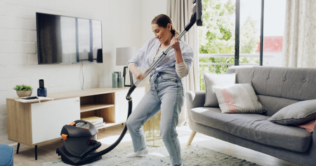 Woman, vacuum cleaner and air guitar in home, happy and playful with music, hygiene and routine. Person, smile and appliance for dust, carpet or equipment for performance with dance in living roomの写真素材