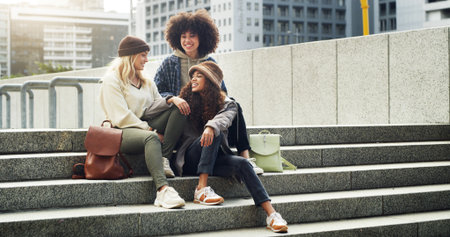 Conversation, city and girl friends on stairs with fashion for trendy, cool and modern clothes on holiday. Happy, steps and female people with stylish outfit in urban town on vacation or weekend tripの写真素材