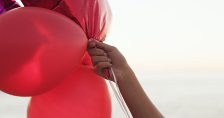 Hand, beach and balloons for love with valentines day celebration, holiday and space outdoor. Romantic gesture, inflatable and person at ocean for care, gift or present on vacation by sea for travelの写真素材