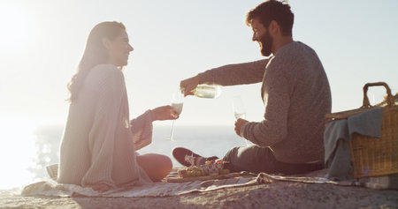 Beach, picnic and couple with love, champagne and bonding together with vacation, relax and romance. Ocean, alcohol and man with woman, anniversary and celebration with summer holiday or relationshipの写真素材