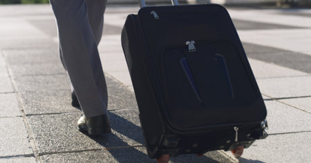 Business travel, suitcase and person in city, legs or journey for job opportunity, walk and outdoor. Back, feet and employee with luggage on urban road, traveller and international trip for seminarの写真素材