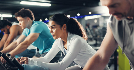 Exercise bike, woman and group in gym for fitness, help or workout for health. Cycling, people and...