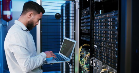 Man, laptop and typing for inspection in server room, hardware and programming for IT solution at...