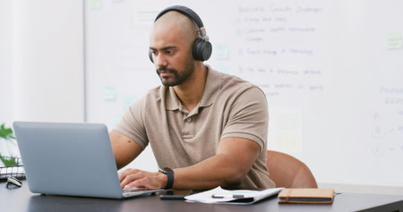 Laptop, headphones and man in office with music, playlist or podcast for working on creative...