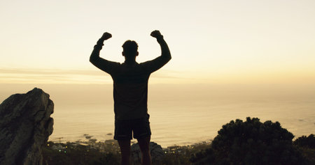 Silhouette, man and winning with fist pump on mountain for conquer, achievement or accomplishment....