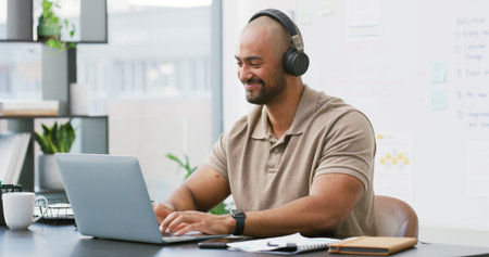 Laptop, headphones and man typing in office with music, playlist or podcast for working on creative...